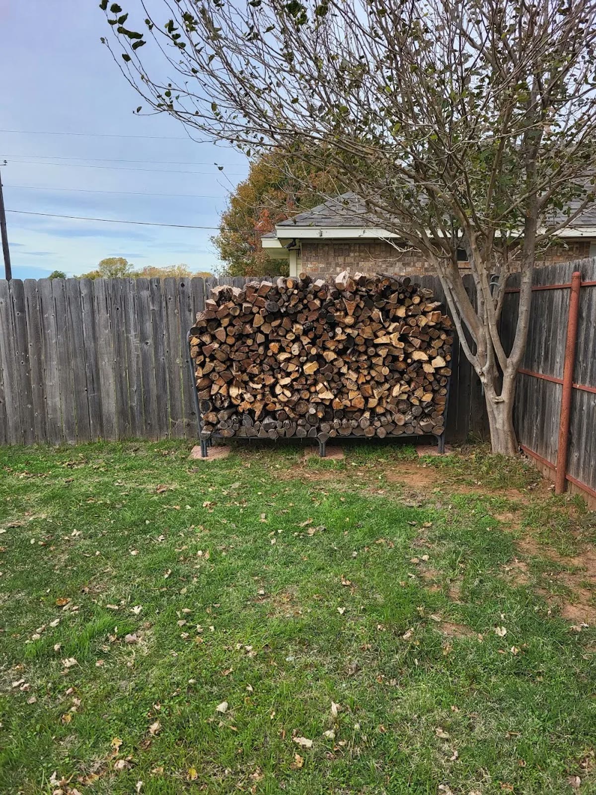 A full rack of stacked seasoned firewood in a Wichita Falls backyard